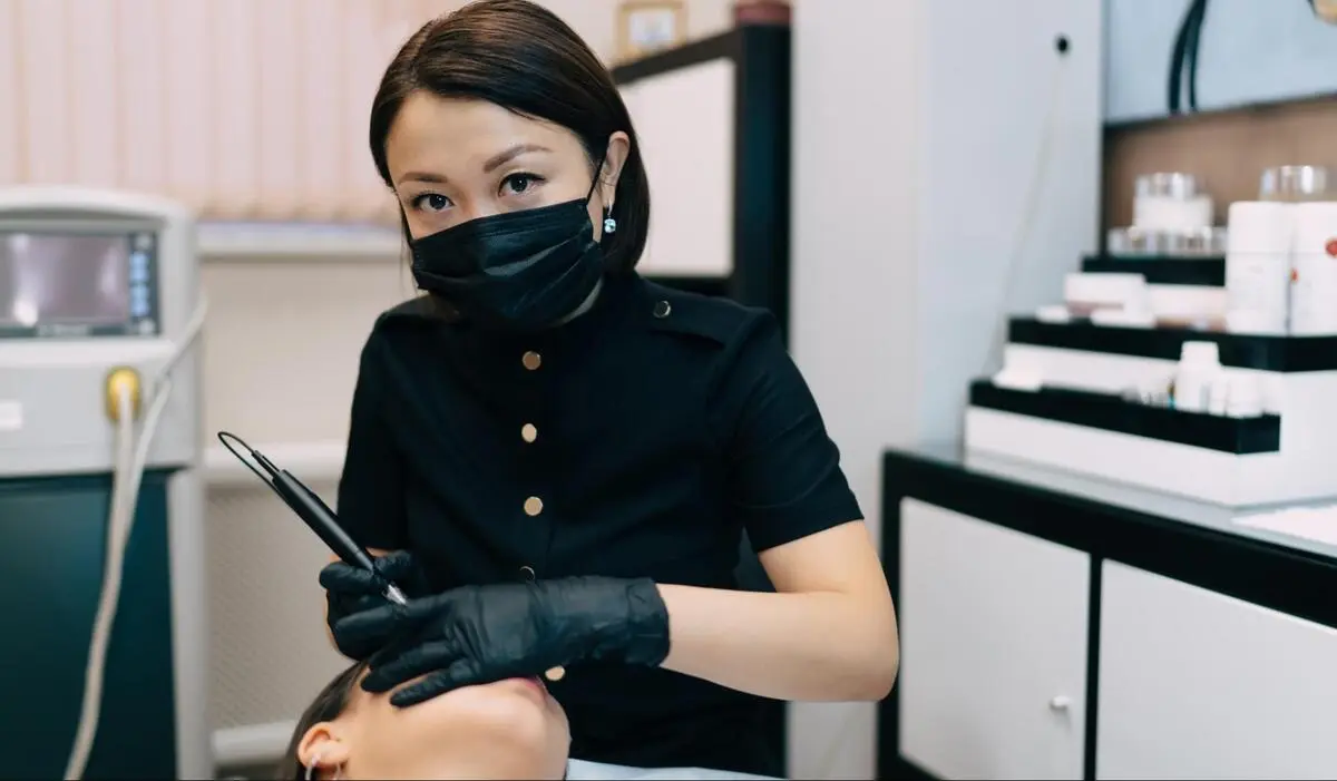 Aesthetic Practitioner with Laser Device - Yellow Laser Clinic Singapore Female aesthetic practitioner in black mask and gloves holding a laser device in a clinical skincare setting in Singapore